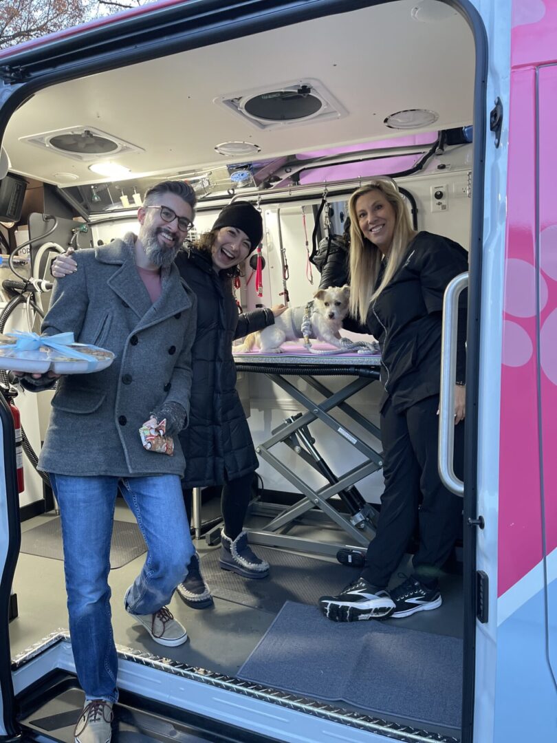 Three people with small dog in grooming van